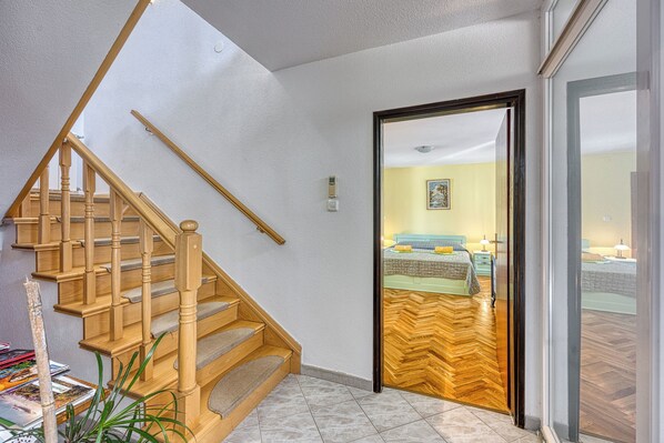 A wooden staircase leading to a bedroom with a bed, bedside tables, and a view through a glass door.