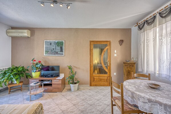 Un salon avec un canapé, un téléviseur, des plantes en pot et une table à manger avec des chaises.