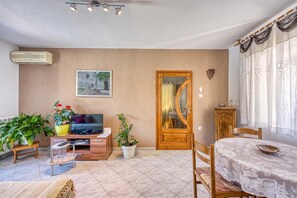 A living room with a television, plants, a wooden door, and a dining area with a table and chairs. - Pool House Klarina (Pican)