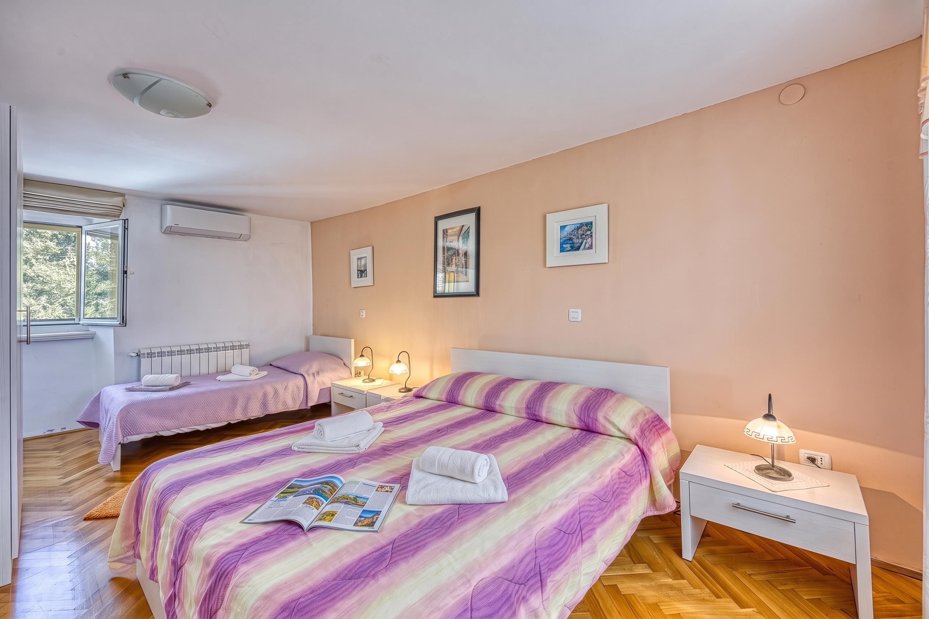 A bedroom with two beds, a radiator, a window, and wall-mounted artwork.