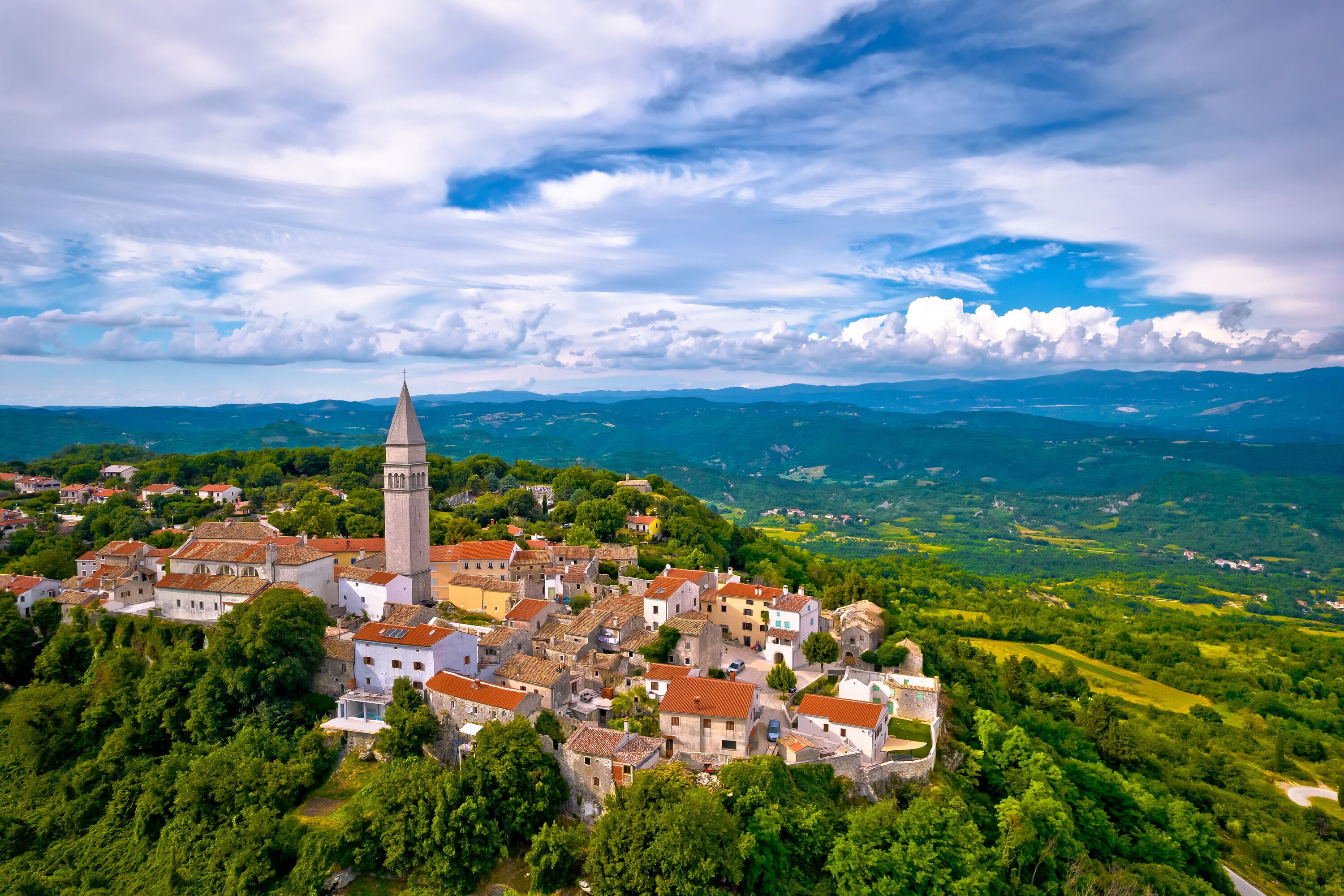 A historic town with a prominent tower, surrounded by lush greenery and rolling hills.