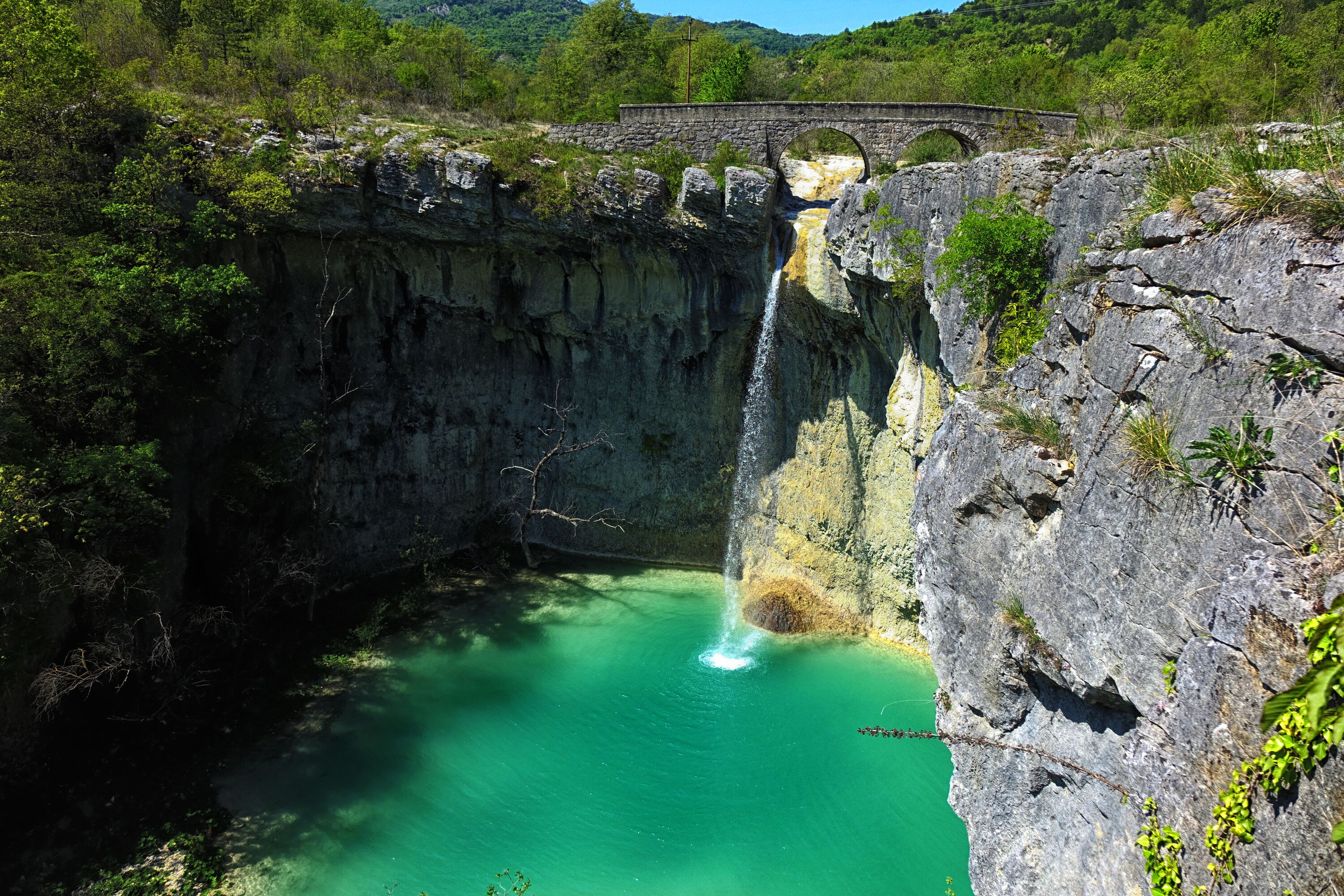 Un puente de piedra sobre una cascada en un entorno natural.
