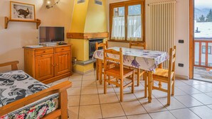 Una habitación acogedora con techo de madera, una chimenea, una mesa de comedor con sillas, un televisor sobre un mueble de madera y una ventana con cortinas.