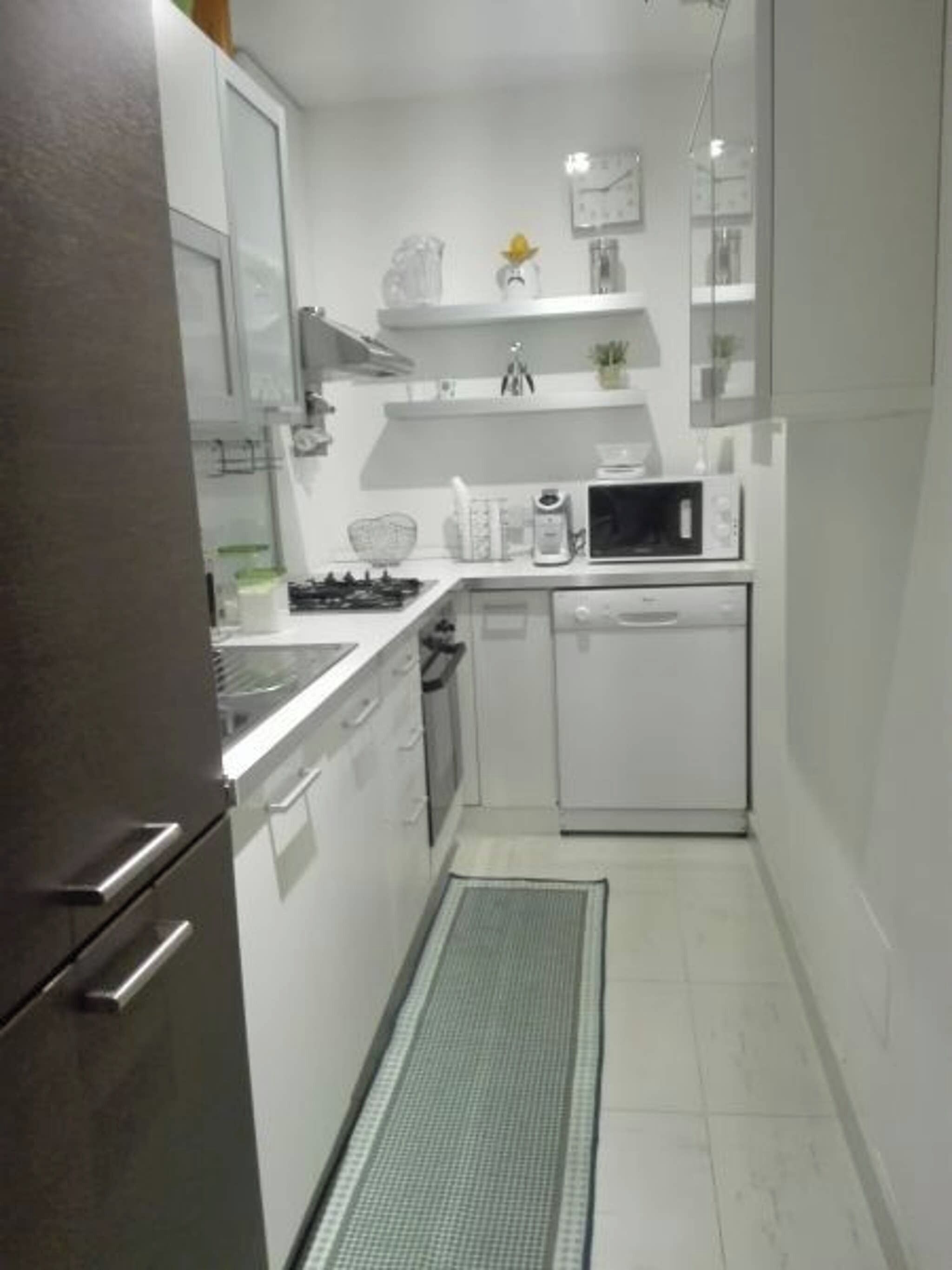 Una cucina compatta con pensili bianchi, un forno a microonde, una lavastoviglie e un piano cottura.