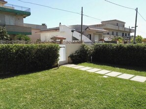 Área residencial com gramado bem cuidado, entrada com portão e casas com varandas e telhados em cerâmica.