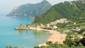 Una zona costera con una playa, un promontorio rocoso y una montaña al fondo.