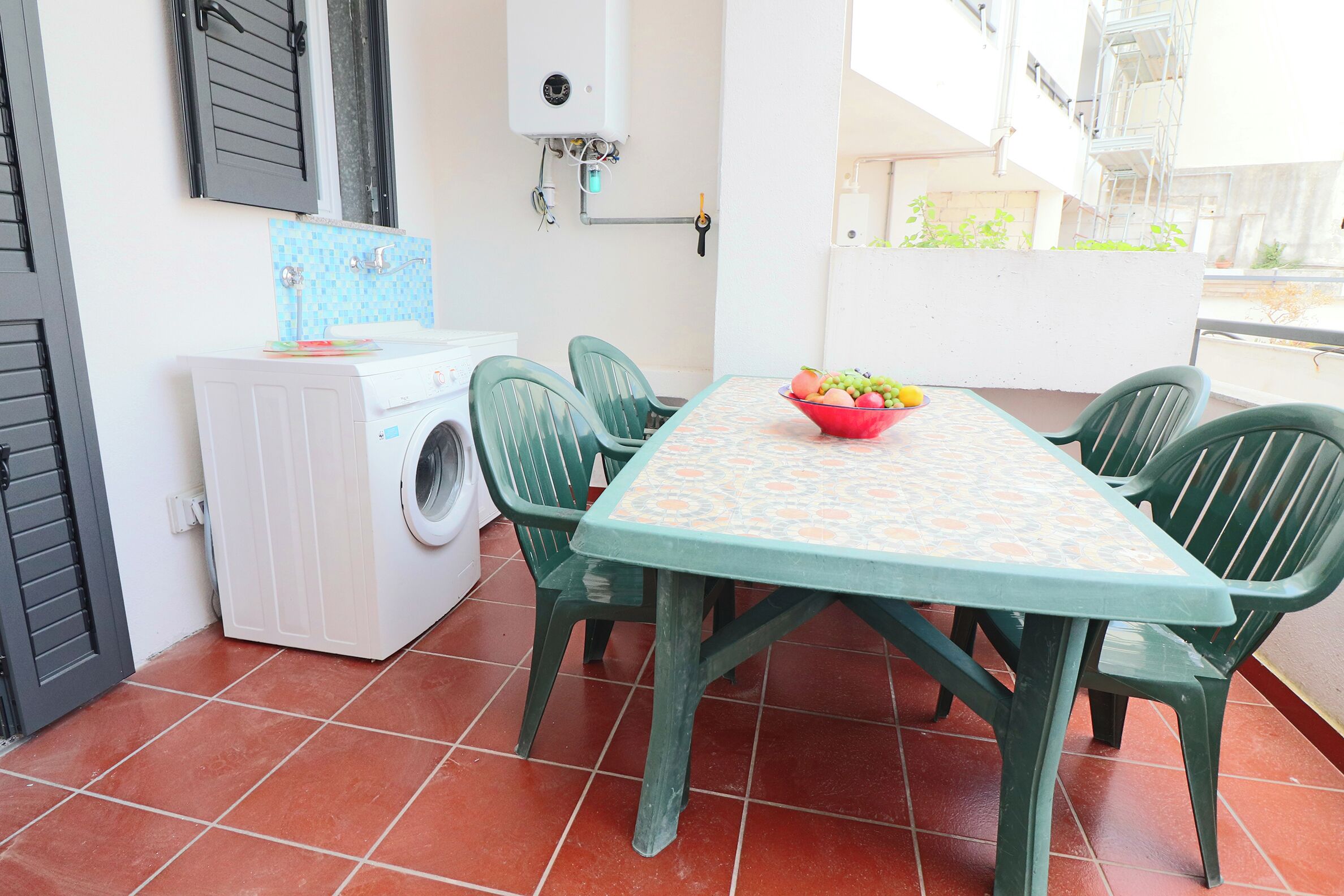 Une petite cuisine équipée d’un lave-linge, d’une table avec des chaises et d’un saladier rempli de fruits.
