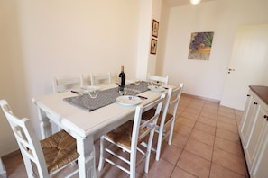 A dining area with a white table, four chairs, a bottle of wine, and a vase with flowers.