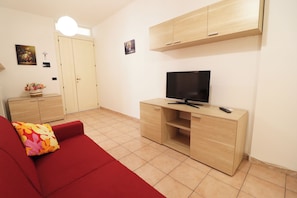 A living room with a red sofa, a TV on a wooden stand, and a light-colored tiled floor.