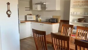 Eine kompakte Küche mit weißen Schränken, einer Mikrowelle und einem Toaster. Ein Esstisch mit Holzstühlen und einer Pendelleuchte sind ebenfalls vorhanden.