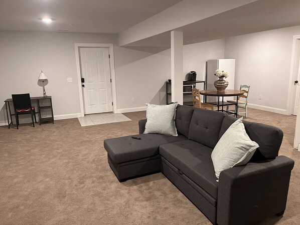 A modern living room with a sectional sofa, a dining table, and a small desk with a lamp.