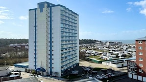 A tall, modern hotel with a flat roof and multiple floors. It is surrounded by a parking lot with several cars and a nearby RV park. - FB06.05 - Modern studio apartment with a view from the 6th floor - Haus Frische (Cuxhaven)