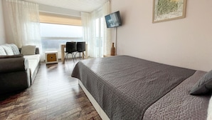 A modern hotel room with a large bed, a desk with two chairs, a TV, and a window with a city view. - FB06.05 - Modern studio apartment with a view from the 6th floor - Haus Frische (Cuxhaven)