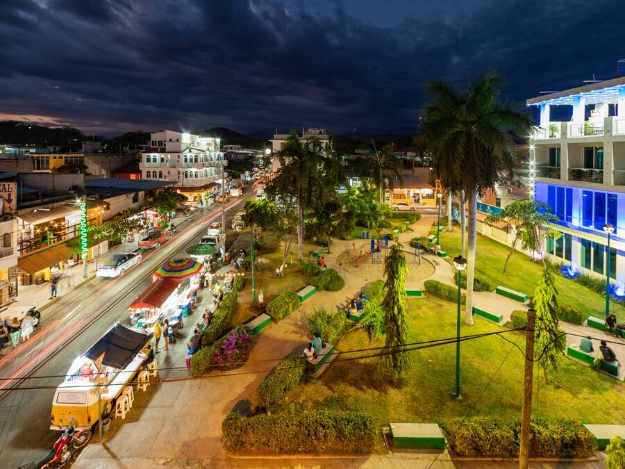 Un paisaje urbano nocturno con una calle bien iluminada, palmeras y edificios modernos.