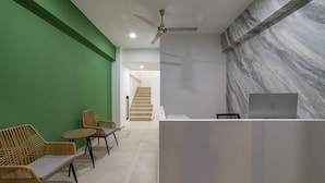 A modern reception area with a white desk, a laptop, wicker chairs, and a staircase in the background.