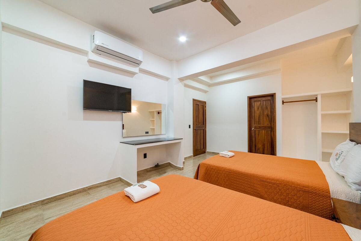 Habitación de hotel con dos camas, televisión, aire acondicionado y armario de madera.