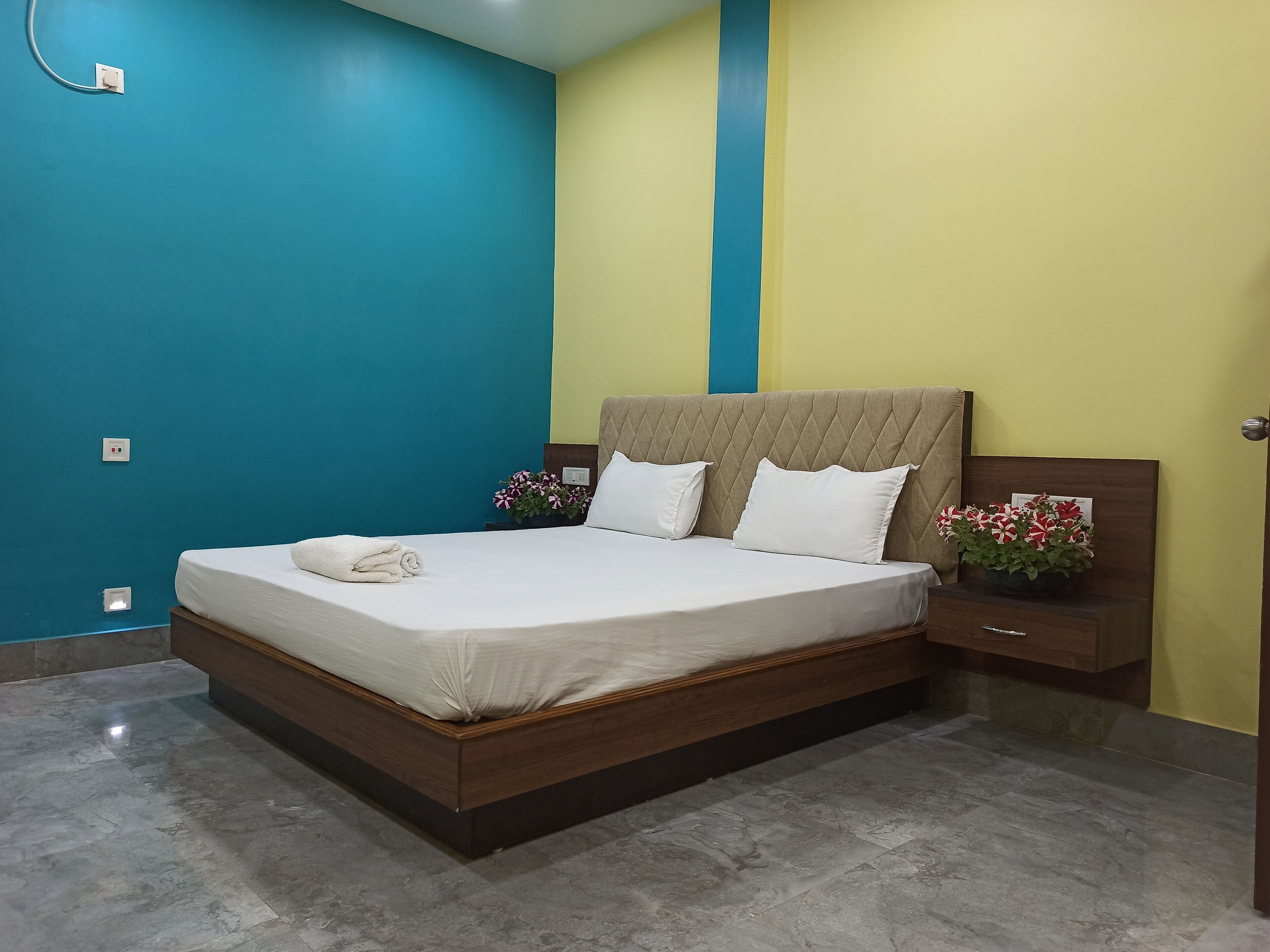 A neatly made bed with white linens, a wooden headboard, and a nightstand with a vase of flowers.