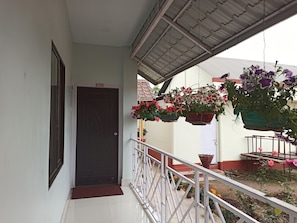 A balcony with a white railing, a dark door, and hanging flower baskets. - Atithya Resort (Sonapur)