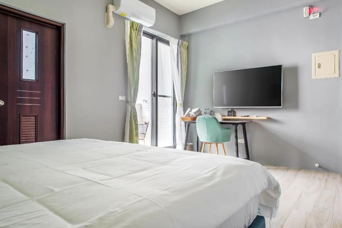 Habitación de hotel con cama, escritorio, silla, televisor y ventana con cortinas.
