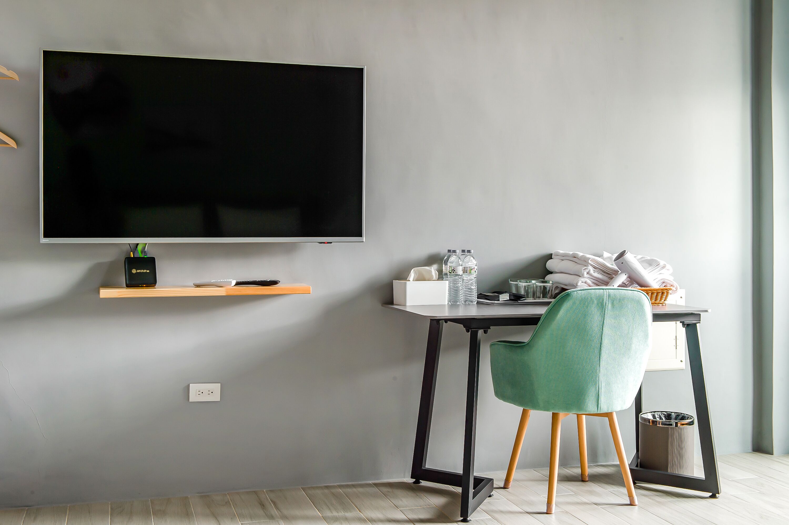 A modern room with a flat-screen TV, a desk with a chair, a trash bin, and a window.