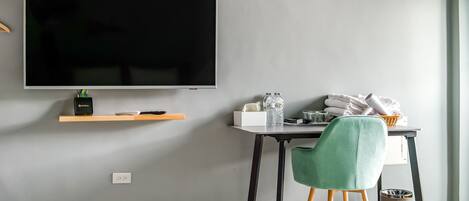 Habitación moderna con televisión de pantalla plana, un escritorio con silla, un cesto de basura y una ventana.