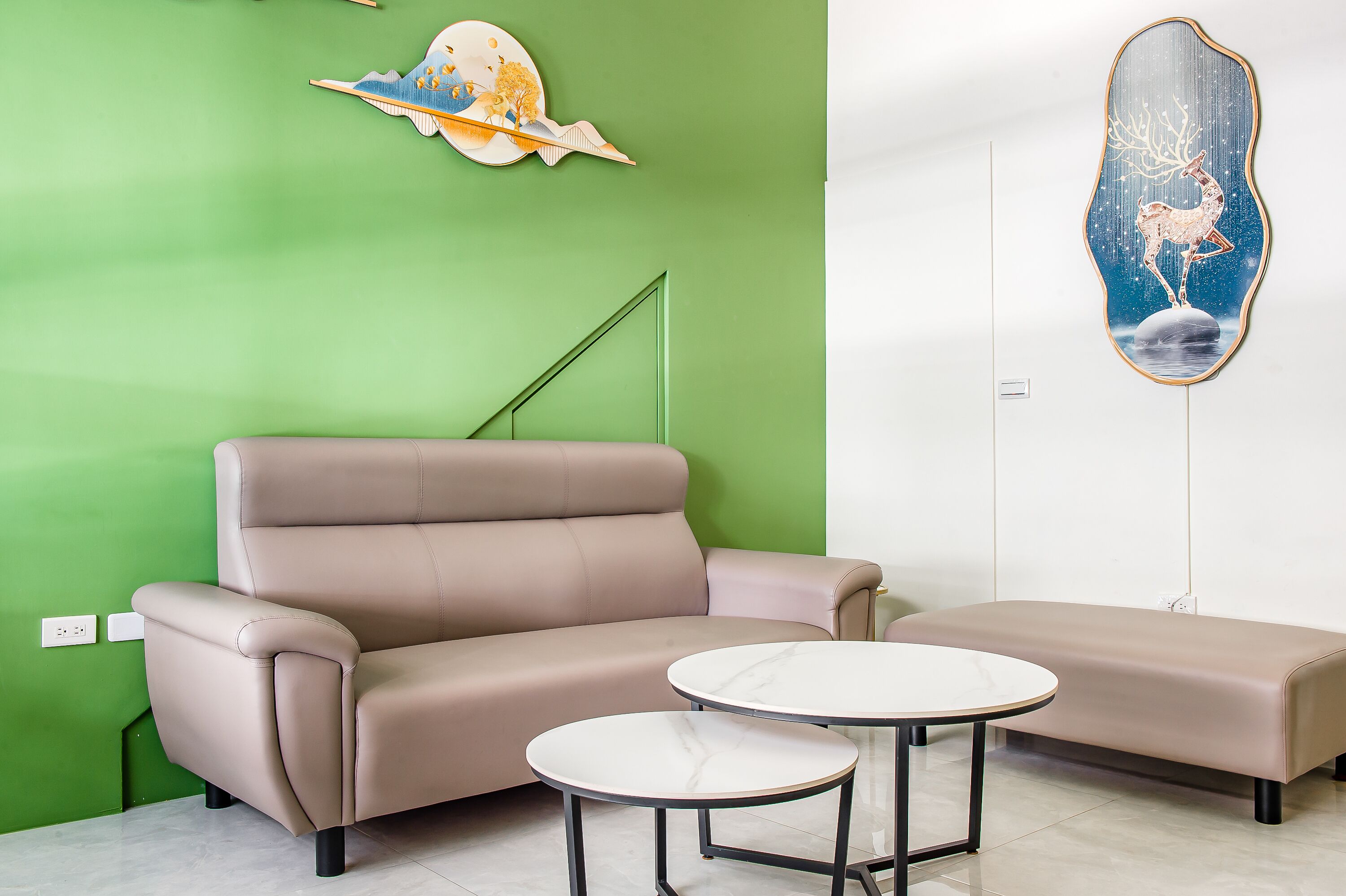 A room with a green wall, a beige sofa, and two round tables.