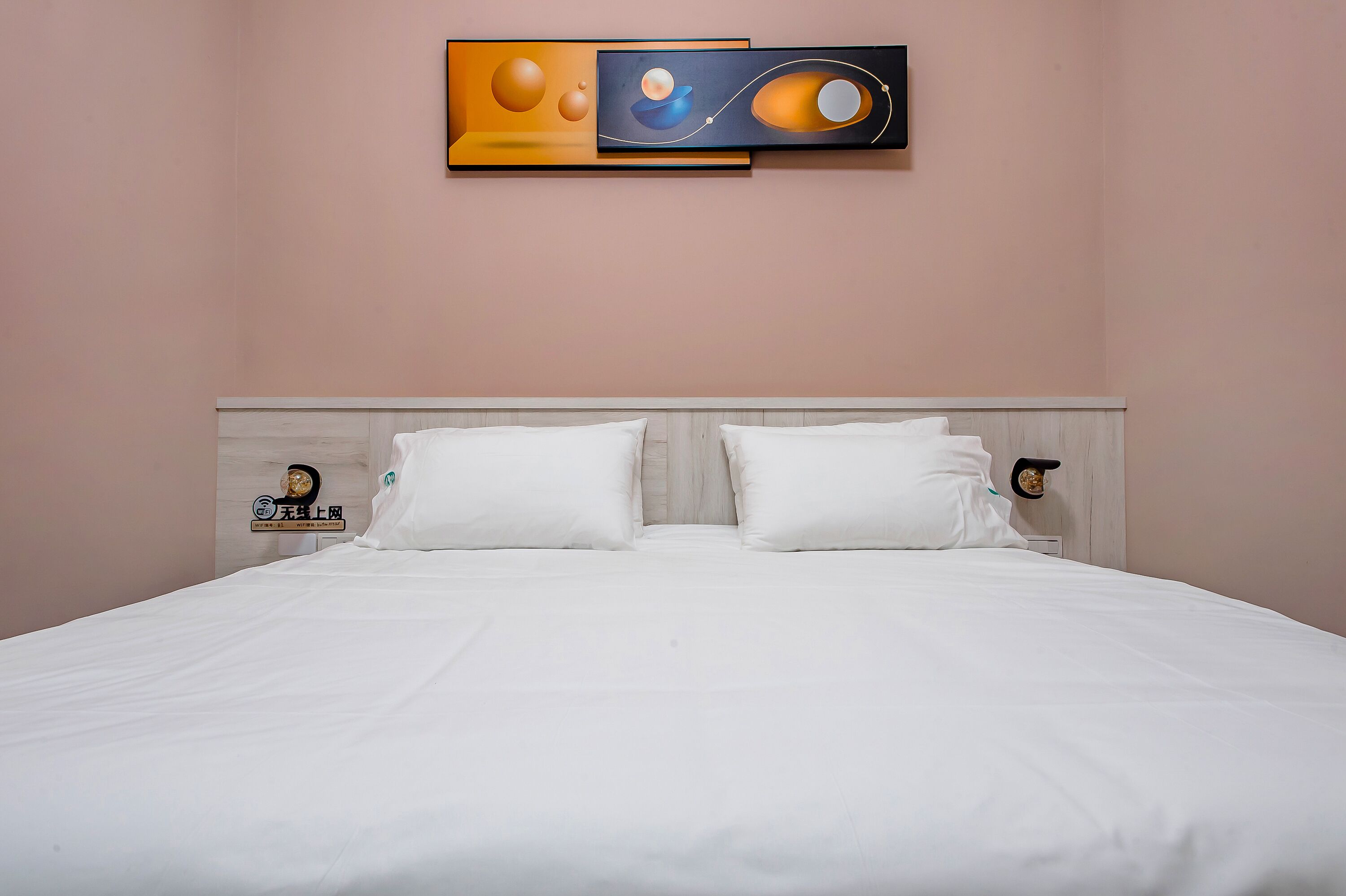 A neatly made bed with white linens and pillows, a light-colored headboard, and a wall-mounted abstract painting.