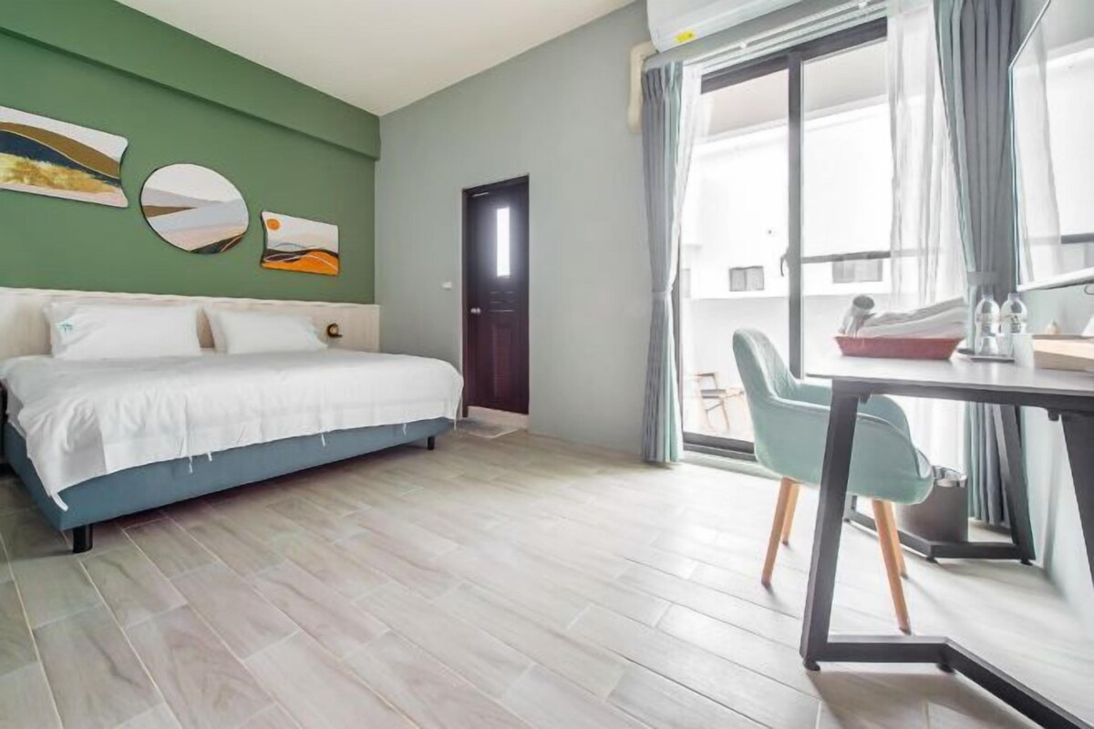 Une chambre à coucher avec un lit, un bureau et des chaises. Il y a une porte et une fenêtre avec des rideaux.