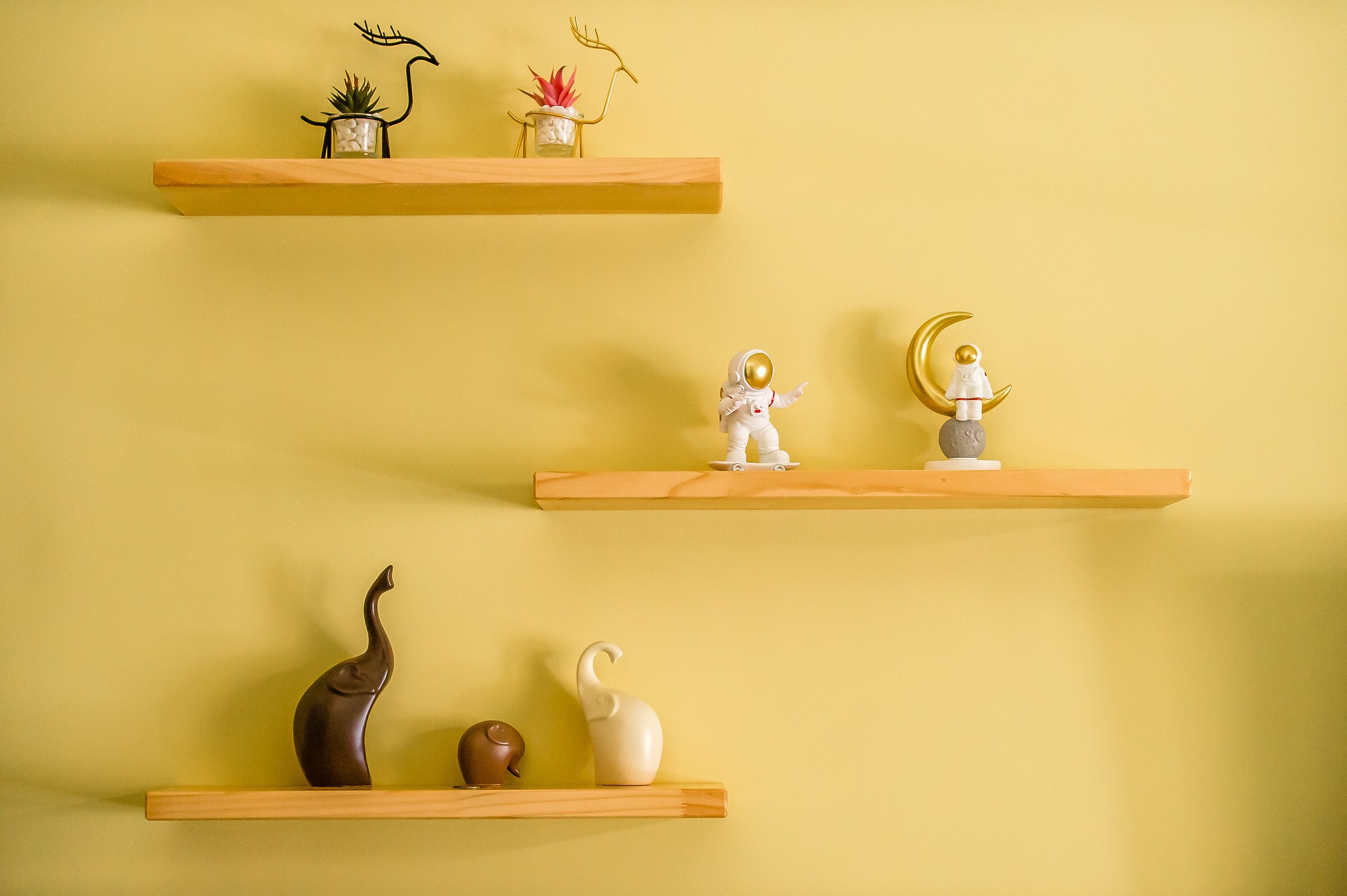 Three wooden shelves against a yellow wall, each holding various decorative items.