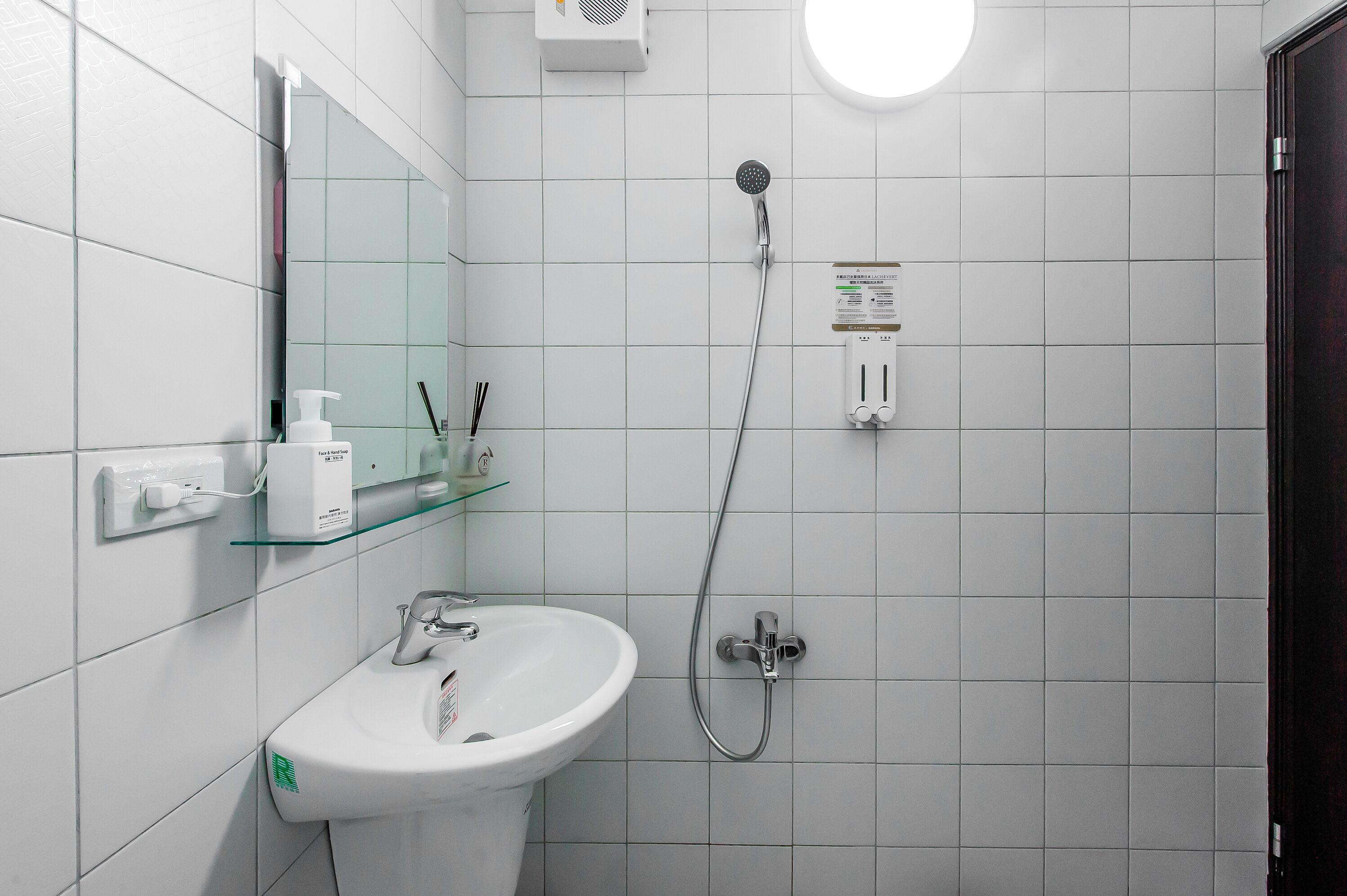 A bathroom with a white sink, a glass shelf, a handheld showerhead, and a mirror.