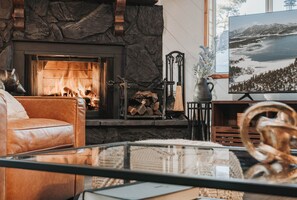 A cozy living room with a stone fireplace, a leather sofa, and a glass coffee table. - Sagewood Cabin 2bed/1.5bath- 1 block from the National forest (Sugarloaf)