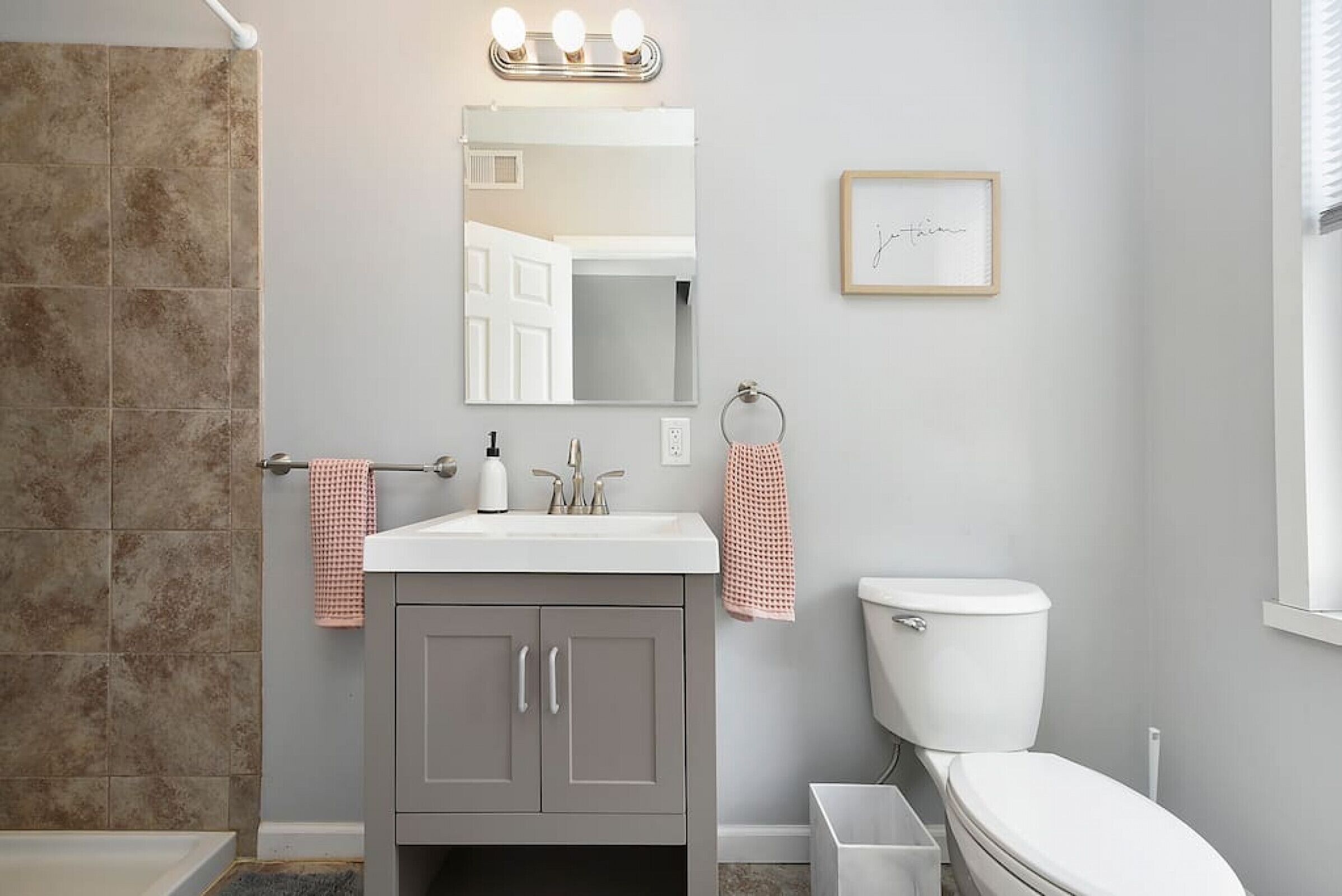 A bathroom with a white sink, grey cabinets, a white toilet, and a shower area.