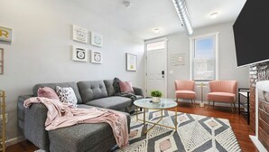 Ett modernt vardagsrum med en grå soffa, rosa fåtöljer, ett soffbord i glas och en mönstrad matta.