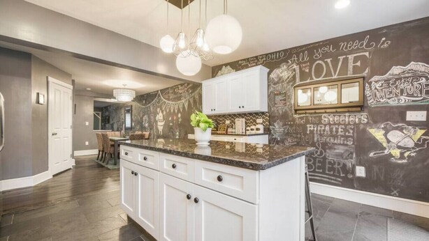 A kitchen with white cabinets, a marble countertop, and a chalkboard wall with various writings and drawings. - M&J - 823 James St. (Pittsburgh)