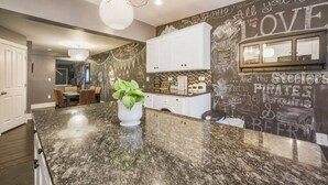 A kitchen with a granite countertop, white cabinets, and a chalkboard wall with sports team names and phrases. - M&J - 823 James St. (Pittsburgh)