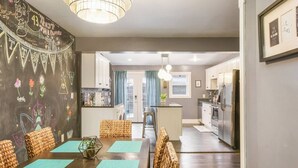 A modern kitchen with white cabinets, a central island, and stainless steel appliances. There is a dining area with a wooden table and chairs, and a living area with a sofa and a coffee table. - M&J - 823 James St. (Pittsburgh)