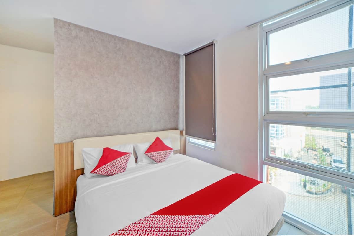 A modern hotel room with a large bed, a window with a view of the city, and a neutral color palette.