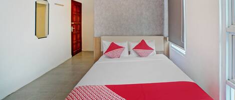 Een hotelkamer met een bed, een raam, een deur en een luchtverkoeler aan de muur.