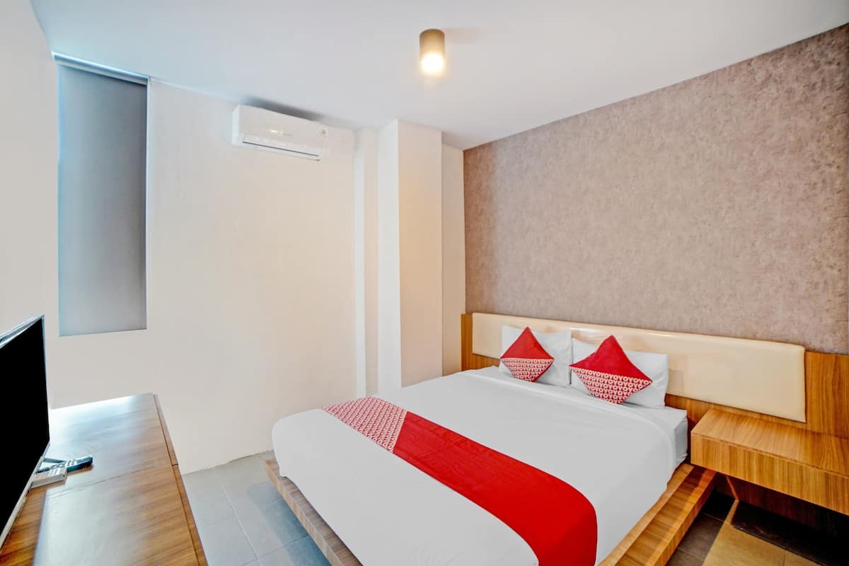 A hotel room with a bed, a TV, a bedside table, and a wall-mounted air conditioner.