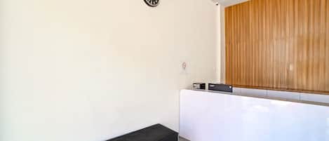 Una habitación moderna con un mostrador de recepción blanco, un banco negro, un reloj y un panel de pared de madera.