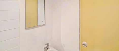 Une salle de bain avec un lavabo blanc, un miroir et une porte jaune.