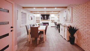 A modern kitchen with a dining area, featuring wooden flooring, white cabinetry, and a brick accent wall.