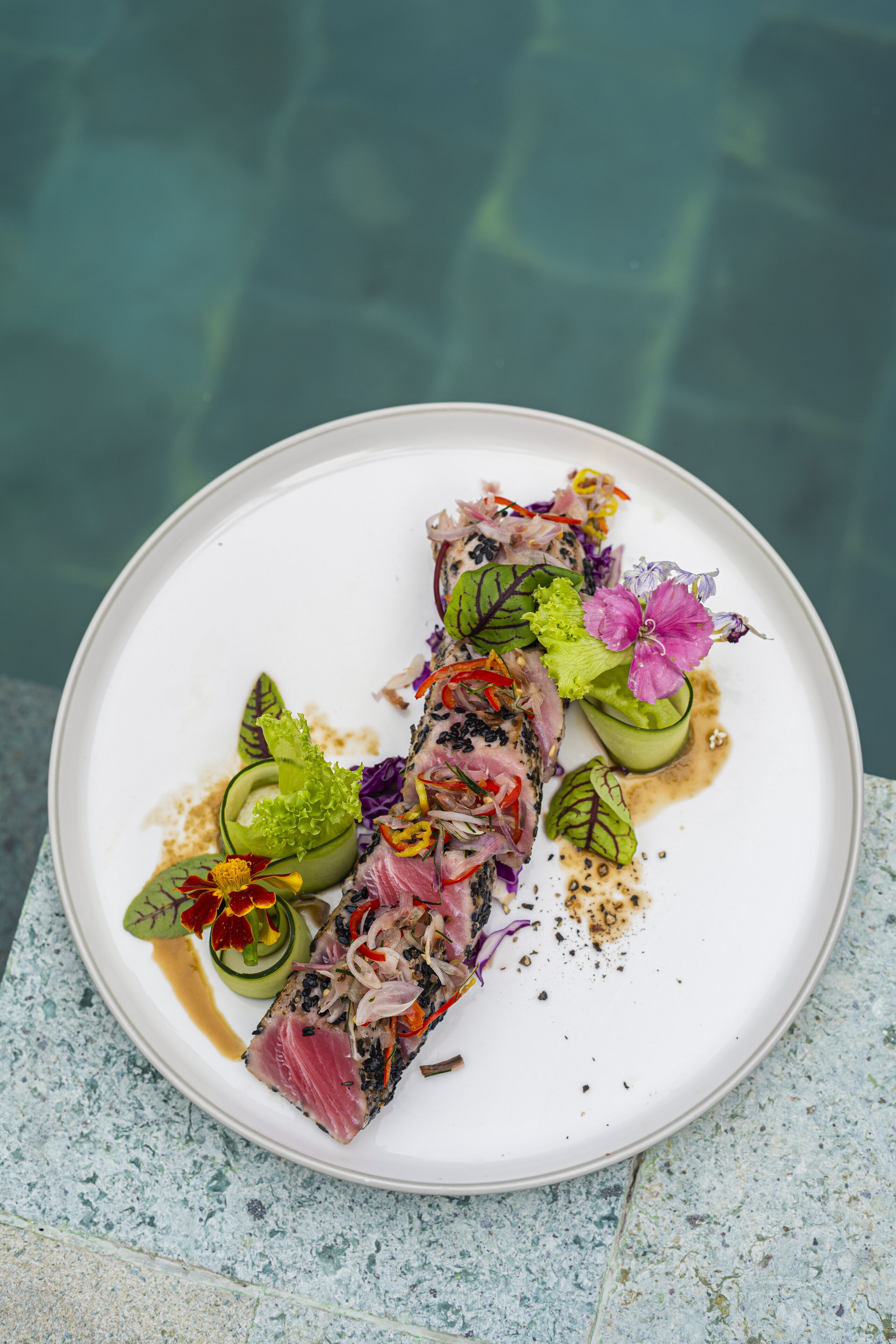 A plate of food with various garnishes and a pool in the background.