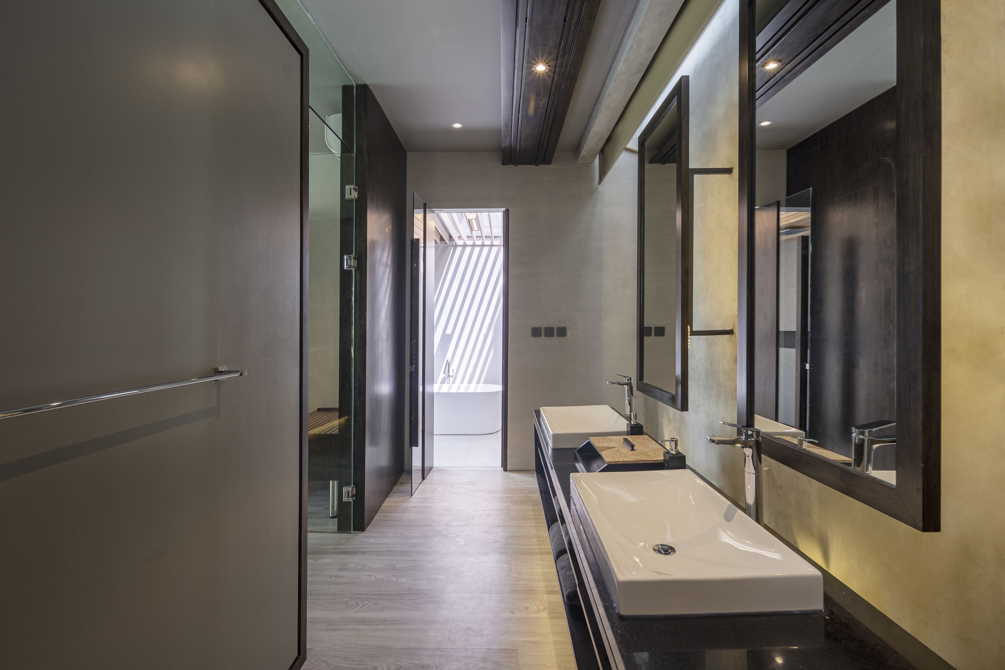 A modern bathroom with a long mirror, two sinks, and a wooden floor.