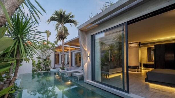A modern house with a glass-enclosed living area, a pool, and tropical plants.