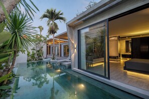 Une maison moderne dotée d’un salon entièrement vitré, d’une piscine et de plantes tropicales.