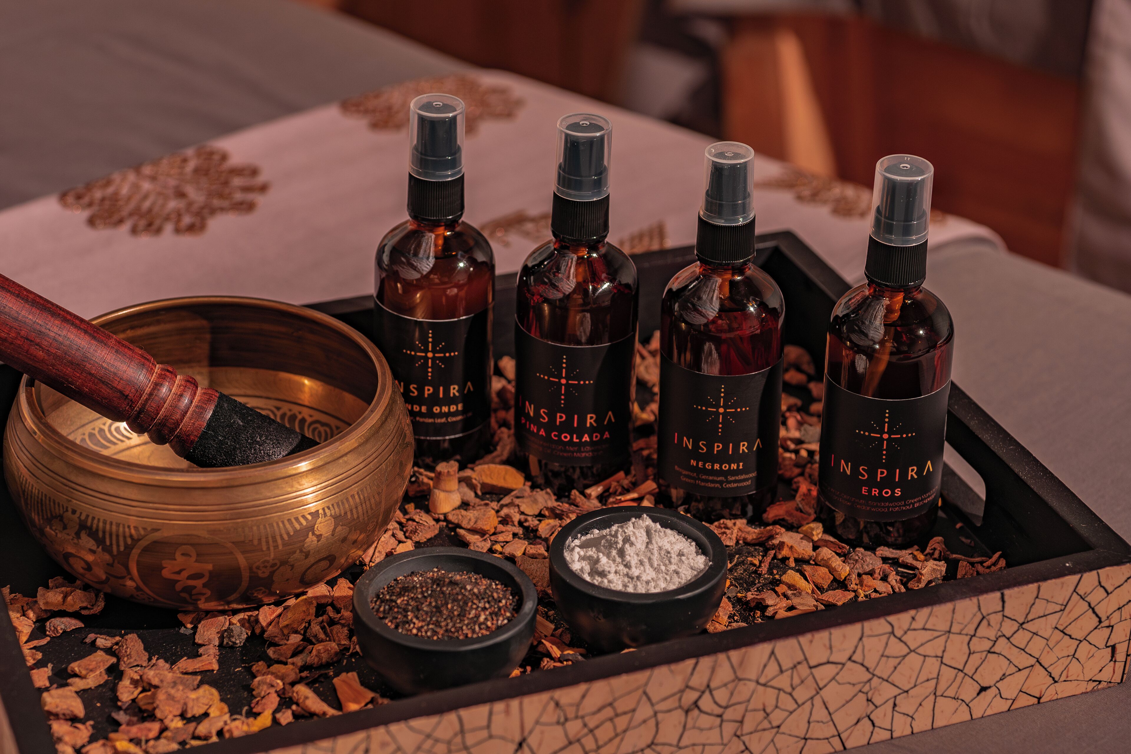 A tray with four bottles of 'Inspira Eros' and a mortar with a pestle, surrounded by various spices and herbs.