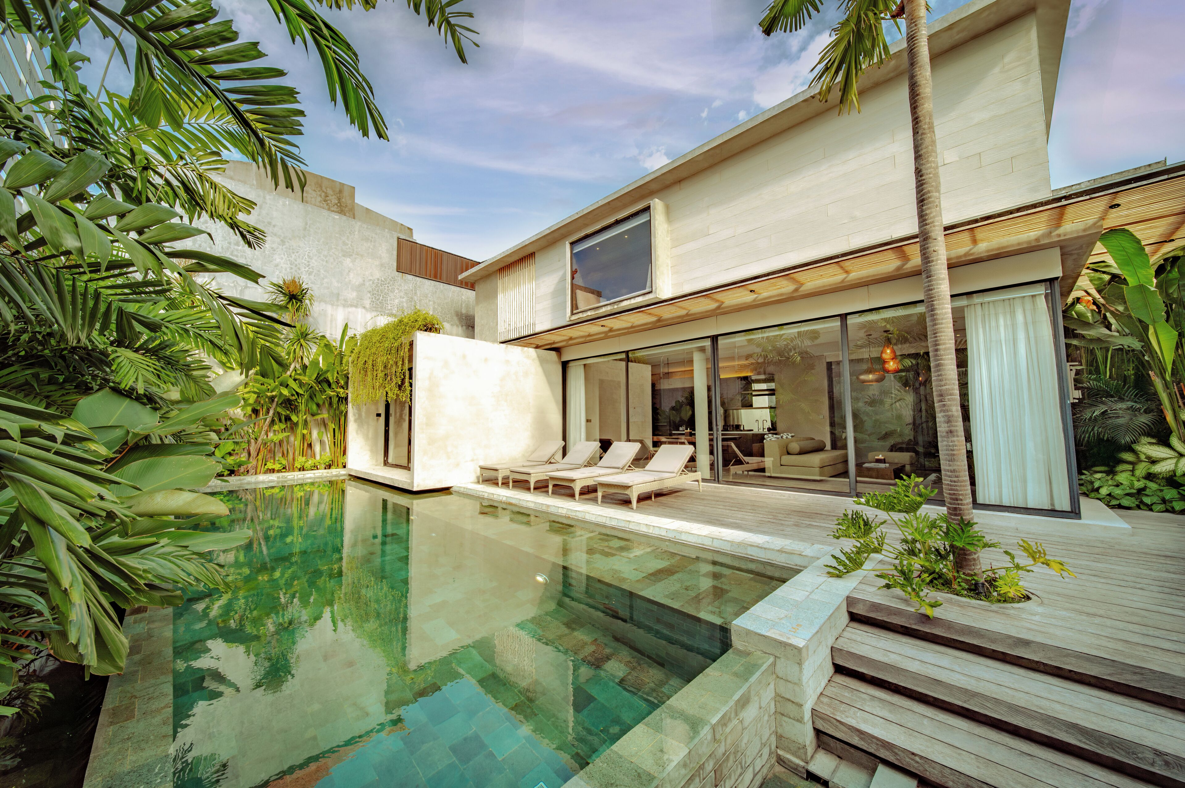 A modern house with a swimming pool, lounge chairs, and tropical plants.