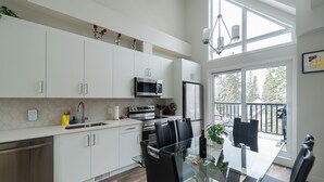 A modern kitchen with white cabinets, stainless steel appliances, and a glass dining table. - Skyline-Townhouse Combo-AC-Pool-Hot Tub (Canmore)