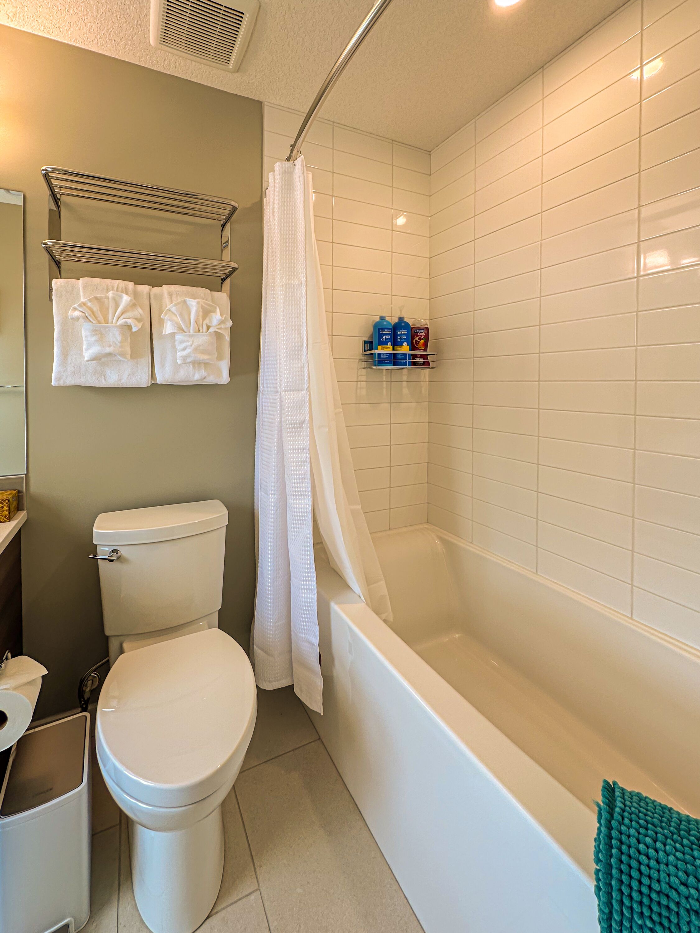 A bathroom with a toilet, bathtub, shower curtain, and a shelf with toiletries.